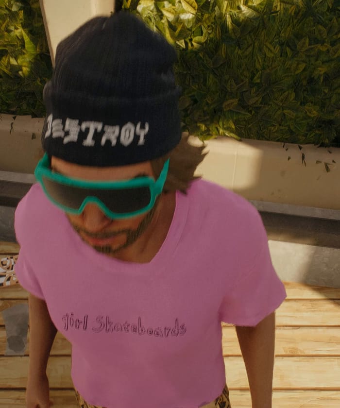 Close-up of a skater in a black beanie, teal goggles and a pink tee.